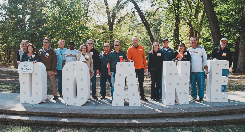 Alumni posing for a photo behind a large Doane sign