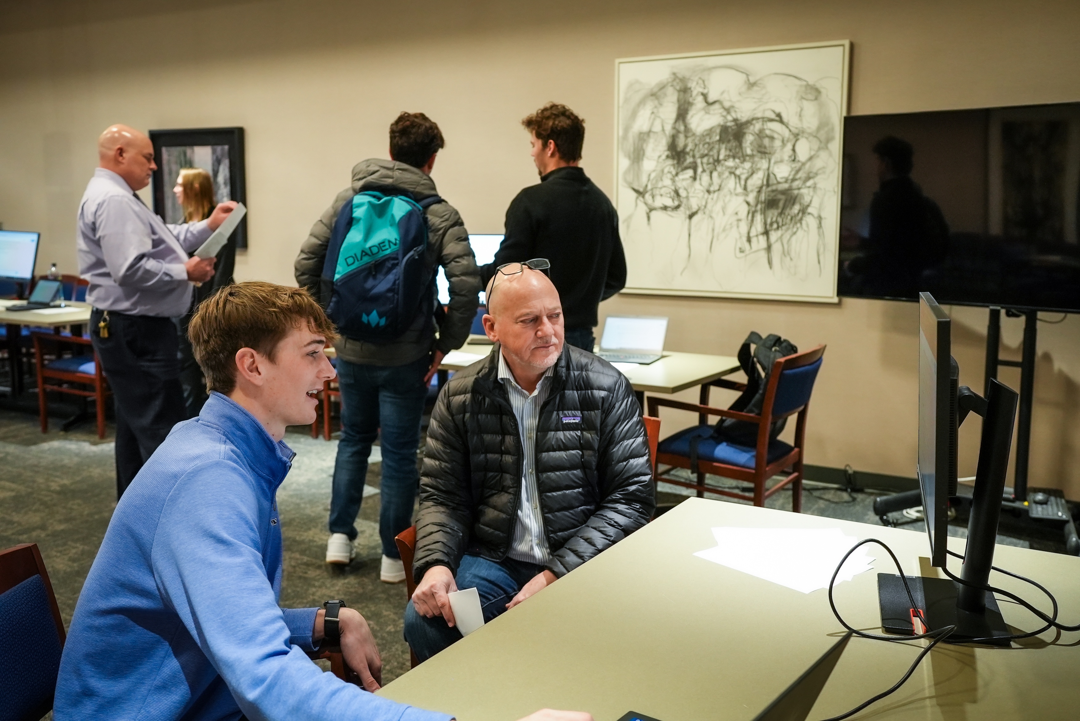 A student shows his project to a professional from the engineering firm Olsson during the AI Showcase