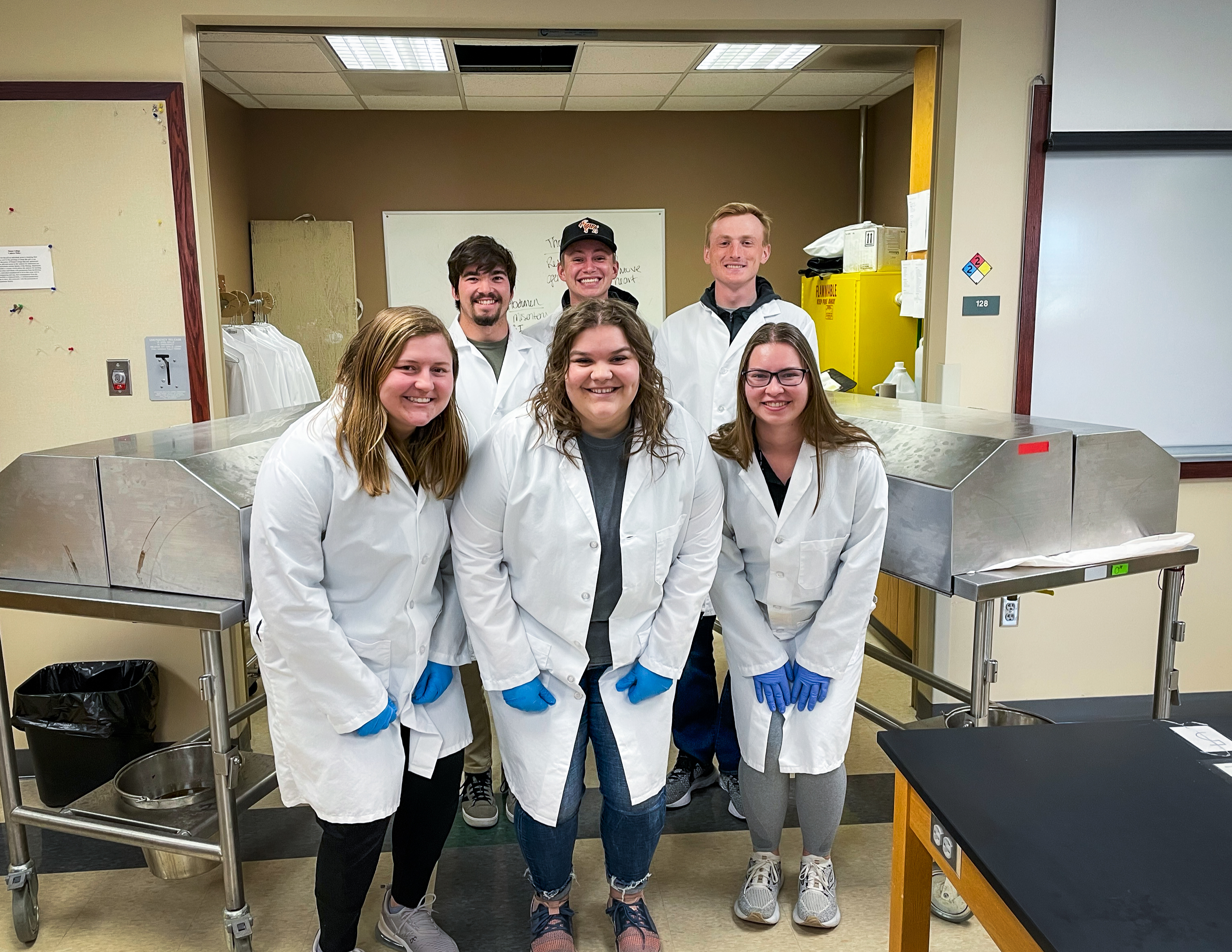 Biology students wearing white coats pose in the lab