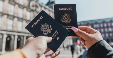 Image by Spencer Davis, through Unsplash. Two people hold up blue U.S. passports in front of an unidentified building. The image shows only their hands and they're holding the passports together in a "cheers" gesture.